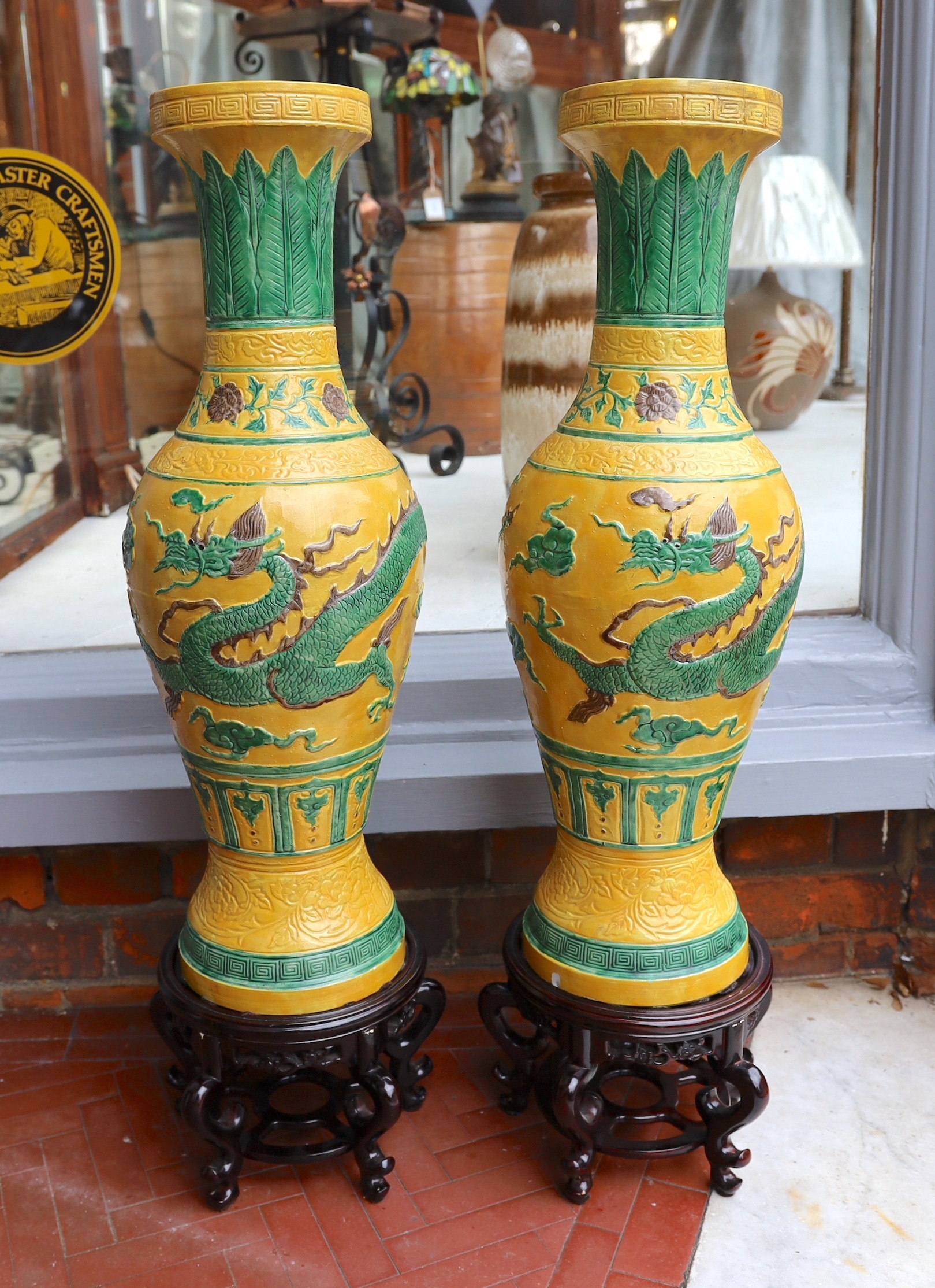 A pair of Chinese yellow glazed baluster vases decorated with bands of flowers and dragons, on hardwood stands, height 67cm. height overall 85cm
